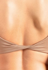 Beżowy top bikini z przodu zawiązanym designem z tyłu, wykonany z gładkiej tkaniny o delikatnym połysku, na tle ukazującej się fakturowanej skóry.