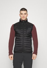 Sort, puffet vest med lynlås foran, høj krave og horisontale kviltede mønstre. Bæres over en mørkerød langærmet skjorte. Holdbart stof.