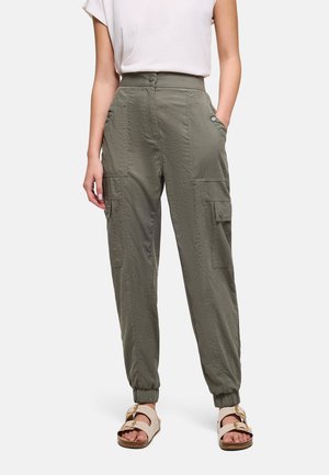 Mujer con pantalones cargo de talle alto color verde oliva con puños elásticos, combinados con sandalias beige con hebilla y una camisa blanca de manga corta metida por dentro.
