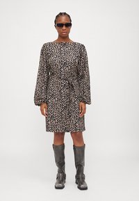 Haljina s leopard uzorkom u bež boji s crnim detaljima, s dugim rukavima, s vezanjem u struku i sivoj čizmama do koljena. Glatka tekstura kroz cijelu haljinu.