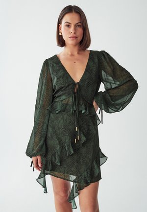 Green animal print dress with V-neck, long puff sleeves, ruffled hem, and tie detail at the waist. Sheer fabric with flowing texture.