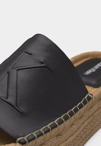 Sandale à enfiler en cuir noir avec un "K" embossé sur la partie supérieure et une semelle plateforme en jute tissé.