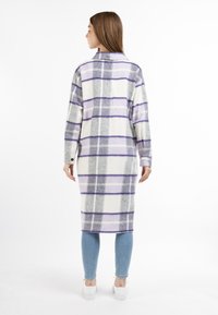 Cappotto a quadri, con maniche lunghe, in flanella bianca, grigia e viola. Caratterizzato da un colletto alto e polsini bottonati, abbinato a jeans azzurri chiari e sneakers bianche.