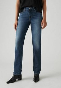 Denim jeans in dark blue, straight-leg design, with subtle fading, five-pocket style, and metal button closure, paired with black ankle boots.