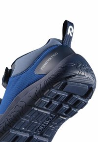 Zbliżenie niebieskiego buta Reimatec z teksturowaną podeszwą, pętlą na pięcie z literą "R" oraz górą z tkaniny z nazwą marki z boku.