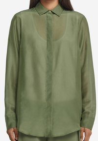 Chemise légère verte avec un devant boutonné, des manches longues et un col classique. Tissu transparent à texture lisse et ourlet incurvé.