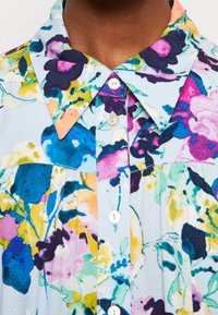 Blommig skjorta med knappar som har en ljusblå bakgrund, livfulla flerfärgade mönster och en standardkrage med vita knappar.