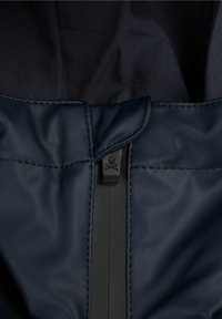 Nærbillede af en marineblå jakkes lynlås med et dødningehoved og knokler-symbol på lynl�åsens træk. 