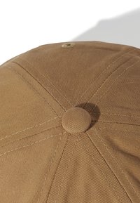 Boné de algodão castanho com uma coroa arredondada, seis segmentos e um botão no topo. Apresenta um tecido texturizado e costura em contraste.