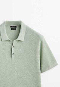 Hellgrünes, strukturiertes Strick-Polohemd mit kurzen Ärmeln, Kragen und Zwei-Knopf-Leiste, flach auf einem weißen Hintergrund präsentiert.