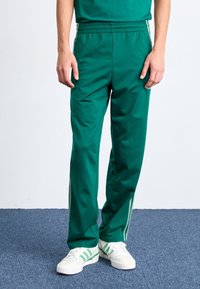 Gröna sportbyxor med avslappnad passform, elastiskt midjeband och sidostreck. Tillverkade av ett smidigt tyg, i kombination med vita och gröna sneakers.