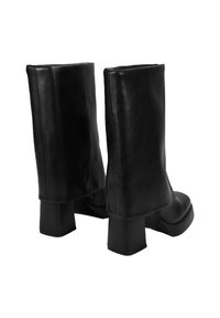 Botas cortas de cuero negro con un tacón grueso y un diseño de parte superior doblada. Textura suave con un detallado mínimo y una silueta elegante.