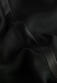 Czarny materiał z teksturowaną powierzchnią, wplecioną w gładką, satynową wstążkę, co tworzy subtelny kontrast w wykończeniu.