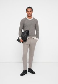Pullover cinza de malha com um colarinho creme, calças bege ajustadas e sapatos de couro pretos. A figura segura uma bolsa de couro preta.