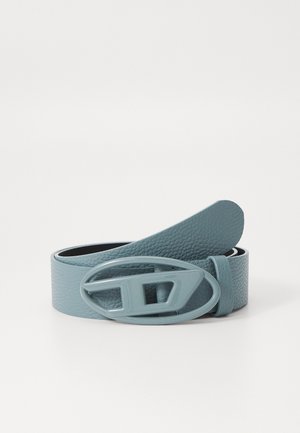 Ceinture en cuir texturé bleu clair avec une boucle en plastique de forme ovale posée enroulée sur une surface blanche.