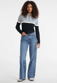 Maglione a treccia grigio, blu navy e bianco con colletto zipper; abbinato a jeans a vita alta, blu chiaro e scarpe grigie.