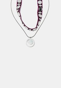 Halskette mit einer metallischen Kette und einem zentralen runden Anhänger, der mit einem lila Textilband geschmückt ist, das mit reflektierenden Scheiben in unterschiedlichen Formen verziert ist.