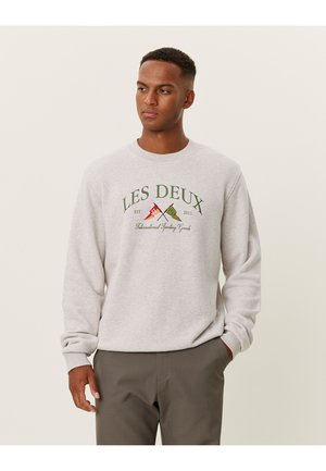 Sweatshirt cinza claro com mangas longas, punhos canelados e decote redondo. Apresenta um texto gráfico colorido com logotipo e duas bandeiras centralizadas.