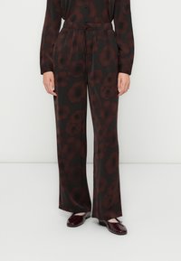 Femme portant un pantalon large noir avec un imprimé floral rouge foncé et un haut à manches longues assorti, accompagné de ballerines bordeaux brillantes.