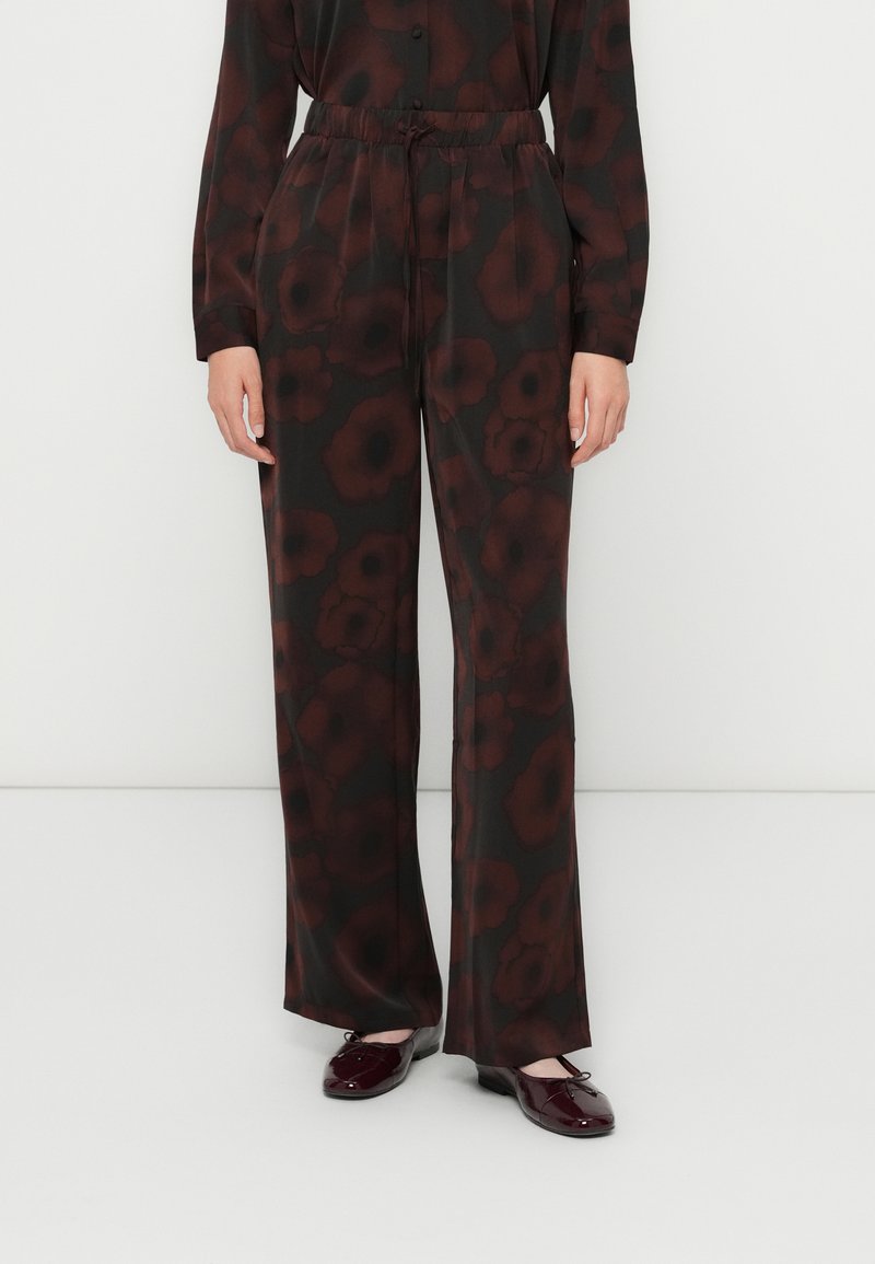 Femme portant un pantalon large noir avec un imprimé floral rouge foncé et un haut à manches longues assorti, accompagné de ballerines bordeaux brillantes.