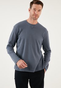 Suéter de manga larga de canalé en azul pizarra, con cuello redondo y un sutil detalle en forma de V en el escote, combinado con pantalones oscuros.
