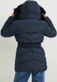 Chaqueta de plumón azul marino con capucha desmontable, ribete de piel sintética, cinturilla elástica y patrón de acolchado en forma de chevron. Corte corto y mangas largas.