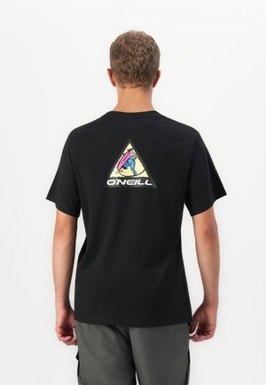 Mand i sort T-shirt med et farverigt trekantet O'Neill-logo med en surfer på ryggen, parret med grå shorts.