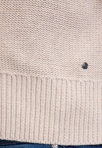 Lichtroze gebreide trui met een geribbelde zoom en een gladde textuur. Voorzien van een klein zwart knoopdetail nabij de zoom.