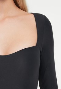 Body noir à manches longues avec un décolleté carré, texture lisse, design ajusté et coutures le long des épaules, mettant en valeur la silhouette.