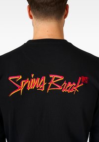 Maglietta nera a maniche lunghe con vivaci scritte ricamate in rosa e giallo che dicono "Spring Break" sul retro, accompagnate da un piccolo logo MTV.