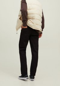 Czarne spodnie o dopasowanym kroju, w połączeniu z kremową kamizelką puchową i ciemnym swetrem. Całość dopełniają czarno-białe sneakersy, co podkreśla swobodny styl.