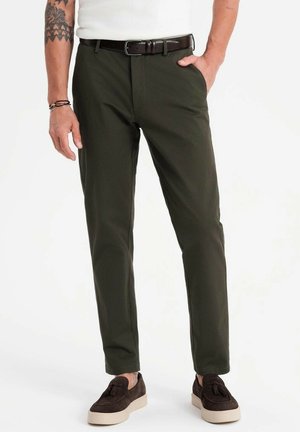 Olivově zelené kalhoty vyrobené z hladkého materiálu, se slim fit střihem, ostrým záhybem a páskem v pase, spárované s tmavě hnědými semišovými botami.