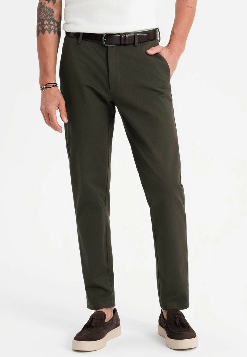 Olivgröna byxor gjorda av ett slätt tyg, med slim fit, skarp vikning och bälte i midjan, i kombination med mörkbruna mockaskor.