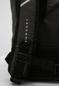 Black waterproof backpack with a sleek design. Features adjustable straps, a reflective strip, and hardware accents. Durable fabric texture.