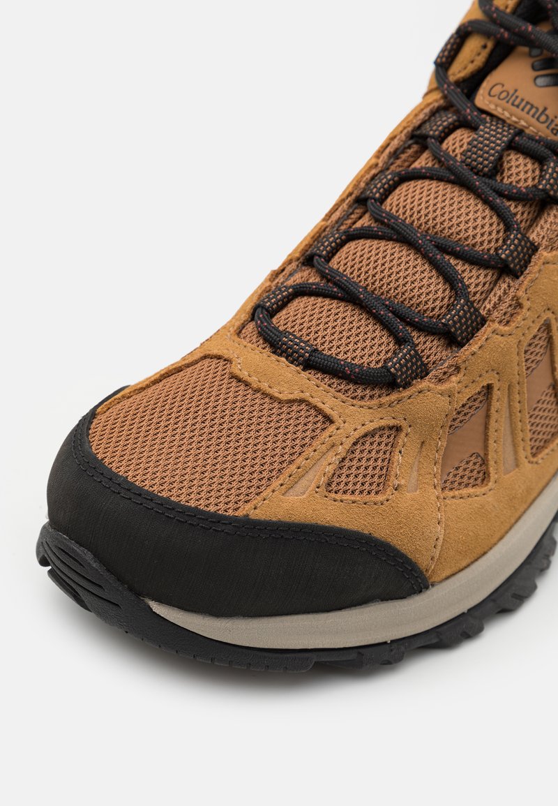 Baskets athlétiques en daim brun et mesh avec un capuchon en caoutchouc noir, finition texturée et lacets noirs. Côtés renforcés pour la durabilité.