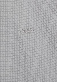 Tissu gris clair avec un motif à carreaux subtil et un petit mot brodé "Swiss" au centre.