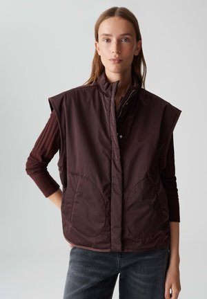 Bordeaux mouwloze vest, gewatteerde stof, hoge kraag, voorzakken en drukknoopsluiting, gelaagd over een geribde lange mouwen shirt.