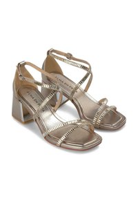 Goldene metallische Sandalen mit Riemchen, einem Blockabsatz, quadratischer Zehenpartie und dekorativen geriffelten Akzenten an den Riemen. Glatte, glänzende Textur.