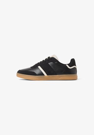 Zapatillas deportivas negras con acabado de cuero liso y gamuza. Presentan rayas blancas y una suela de goma. Diseño de tobillo bajo.