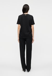 T-shirt preta de algodão com mangas curtas, corte descontraído e decote redondo, combinada com calças pretas largas. Design minimalista, sem padrões.