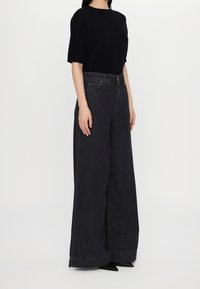 Haut noir à manches courtes associé à un jean en denim foncé à taille haute et jambes larges. Le jean présente une finition soignée et une texture légèrement délavée.