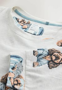 Heledad hall hallilõikega valge puuvillane T-särk, millel on sinised ja persikavidina koera illustratsioonid. Ribitud kaelus, millel on sildikene brändi ja hooldusinfo jaoks.