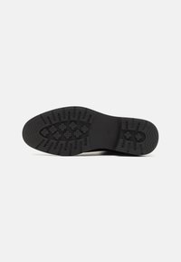 Suela de zapato de goma negra con patrón de tracción texturizado en zigzag y diseños florales en relieve. Área de transición suave cerca del talón.