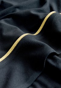 Must mustriga kanga, millel on sile tekstuur, kuldse metallikäärisega lainelise õmbluse ääres. Kanga peal on pehme ja see voolab elegantselt.