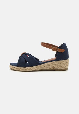 Navy fabric wedge sandals with twisted strap design, brown ankle strap, and jute-wrapped heel, featuring a textured surface.