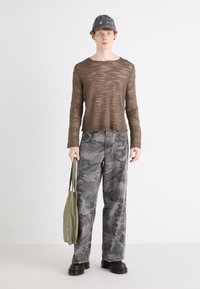 Brun tekstureret langærmet top parret med grå camouflagejeans og sorte platformstøvler. Grøn tote taske hængende på venstre arm.