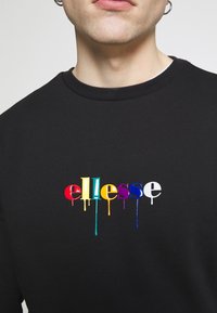 Felpa nera con colletto rotondo che presenta il nome del marchio "ellesse" in lettere colorate gocciolanti: rosso, giallo, verde, viola, blu e bianco.