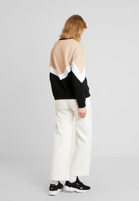 Sweatshirt bicolore en beige, noir et blanc avec un motif en chevron ; associé à un pantalon large blanc et des baskets noires.