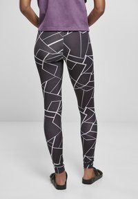 Leggings neri con un motivo geometrico bianco, design aderente e texture liscia, abbinati a una maglietta viola casual.