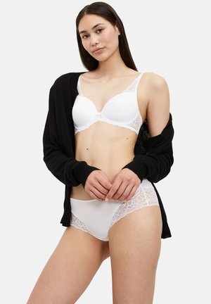 Hvid blonde-bh med matchende trusser. Glat stof med blomsterblonde detaljer på kanterne. Modellen har en sort cardigan på.